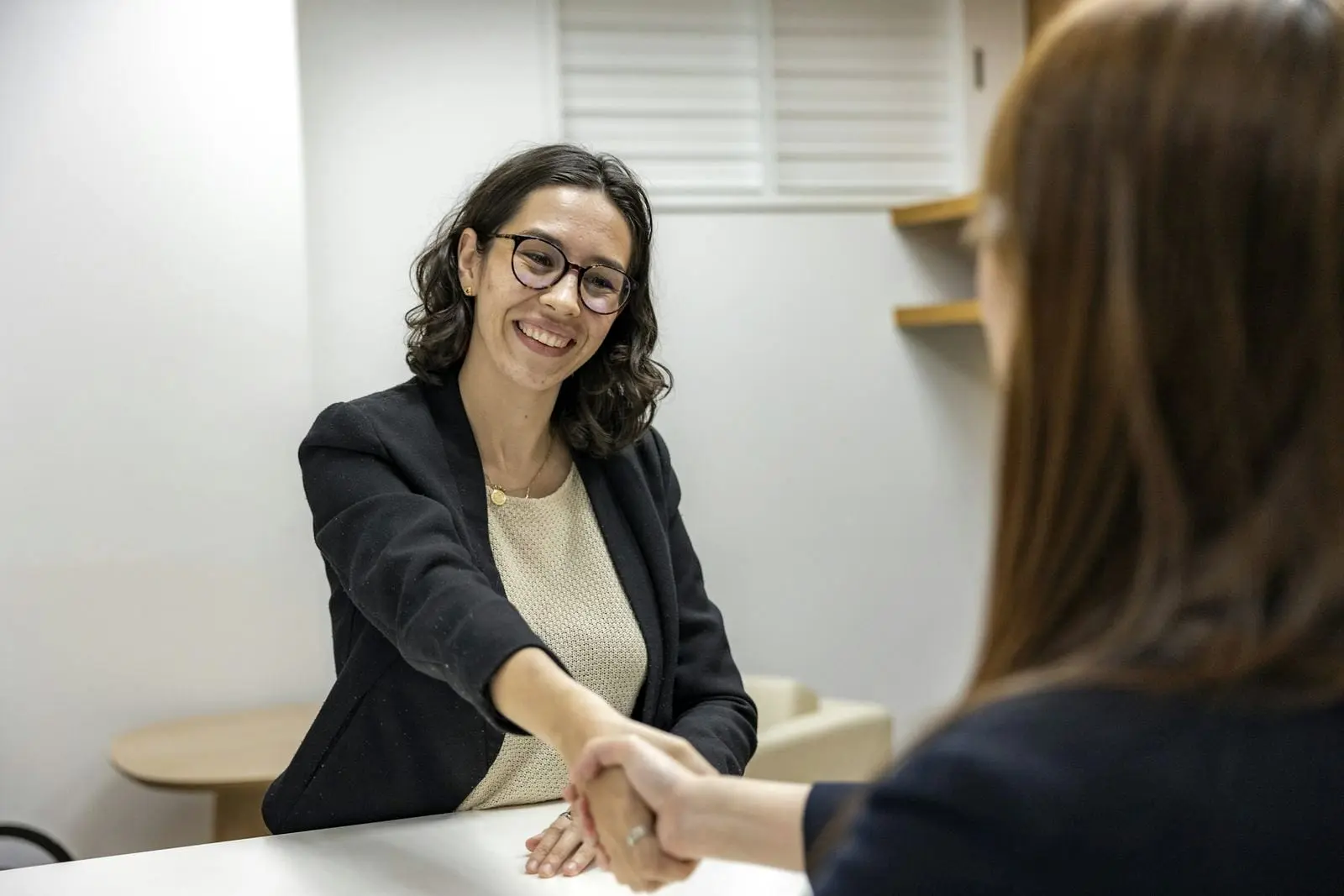 Twee vrouwen geven elkaar glimlachend een hand aan een bureau na een goede afspraak