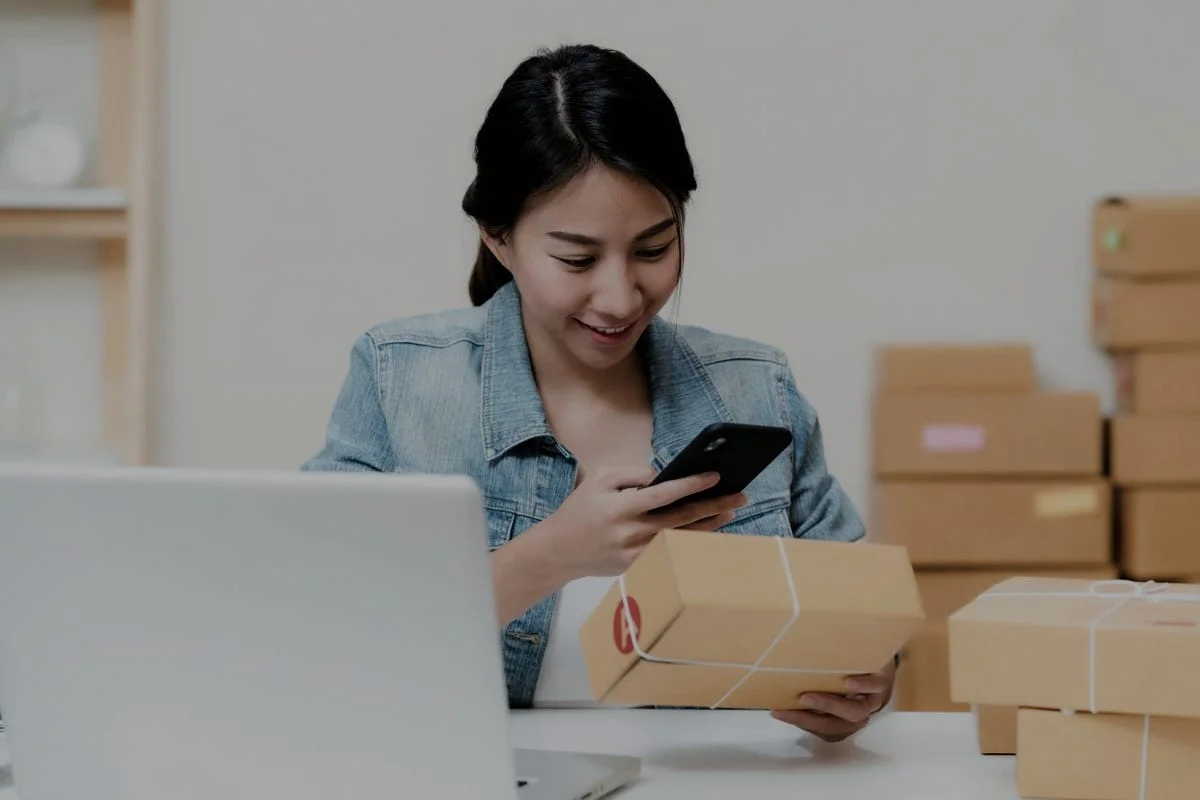 Een webshopondernemer controleert een bestelling op haar telefoon tussen verzenddozen