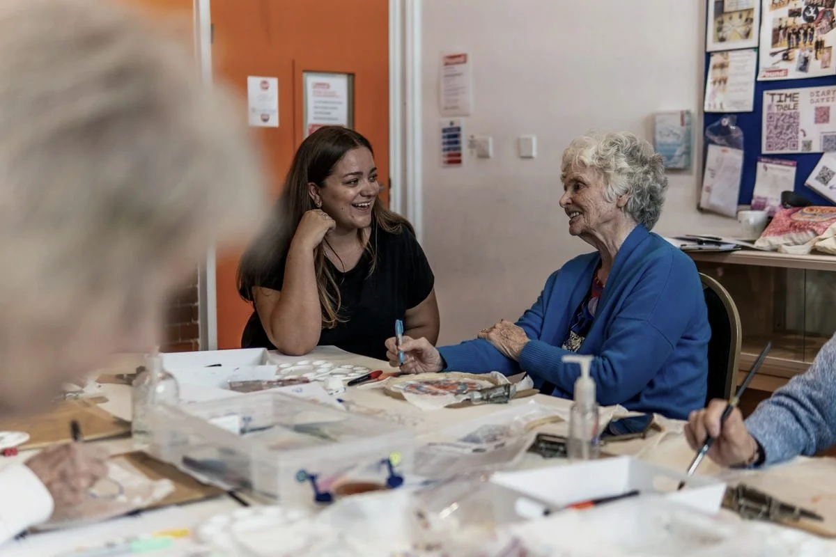 Twee vrouwen zijn samen creatief bezig aan tafel in een buurthuis