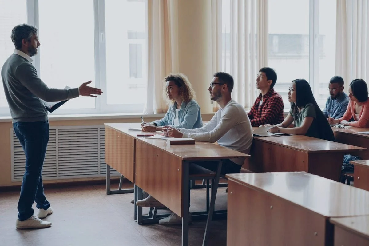 Een docent geeft les aan een groep volwassen cursisten in een lichte lesruimte