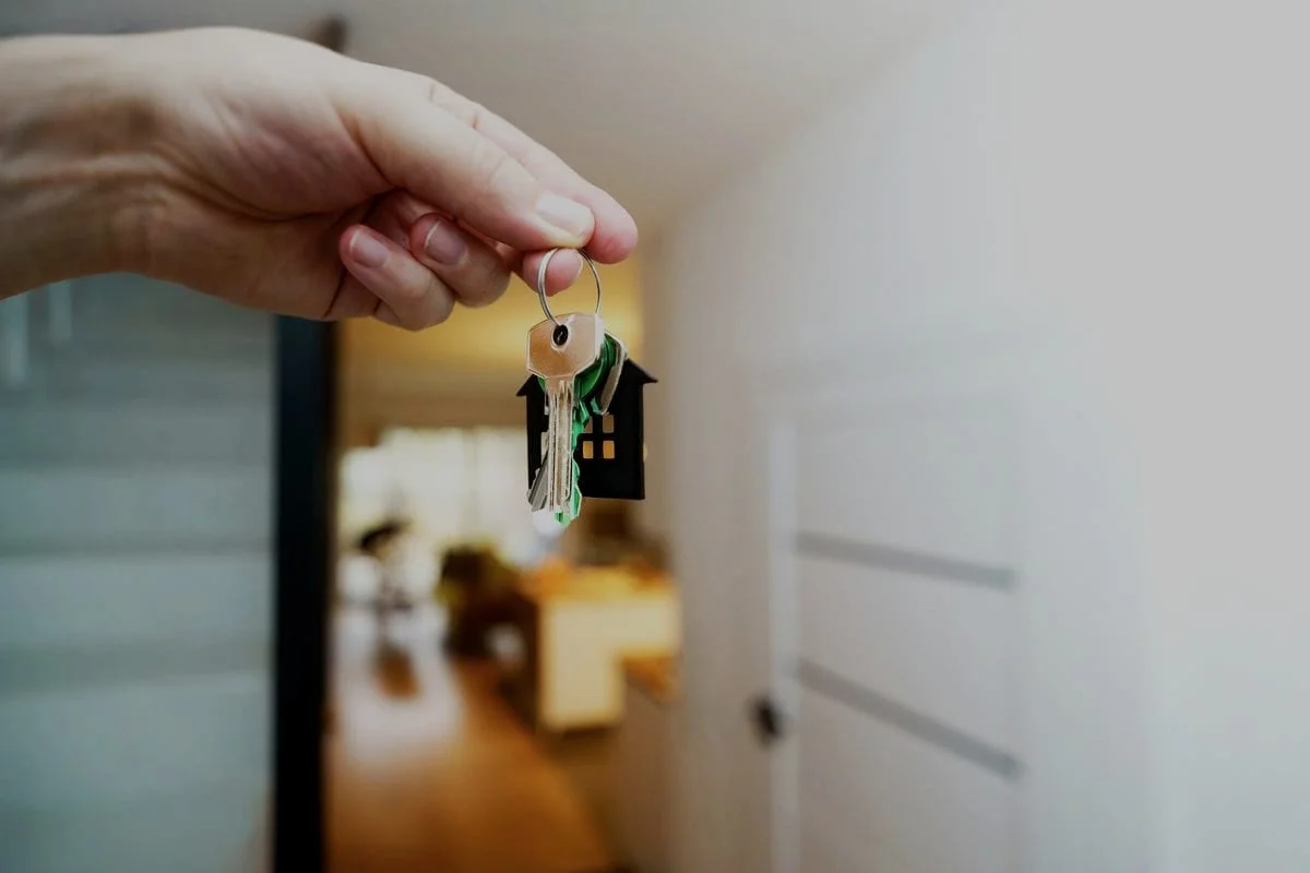 Een hand houdt de sleutels met een huisje als sleutelhanger vast in een woning