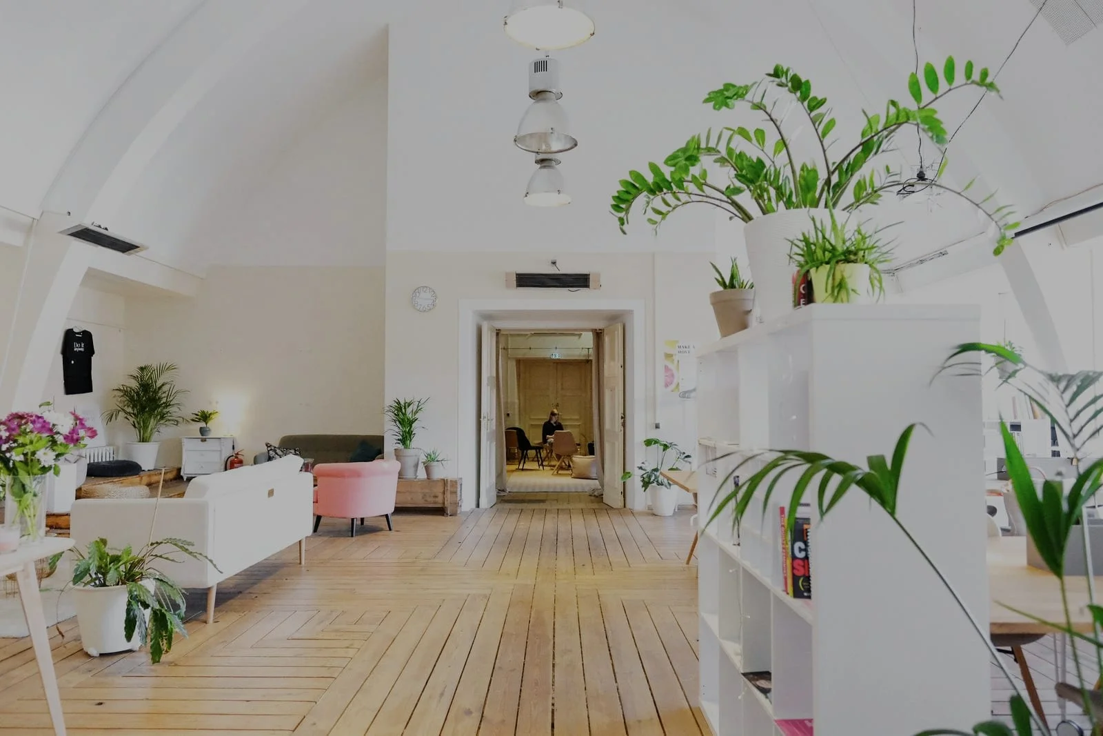 Een lichte, rustige werkruimte met houten vloer, planten en een open doorgang naar achteren