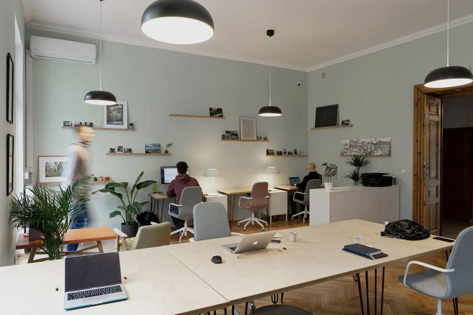 Een lichte flexwerkplek met lange houten tafels, laptops en een paar mensen die rustig aan het werk zijn
