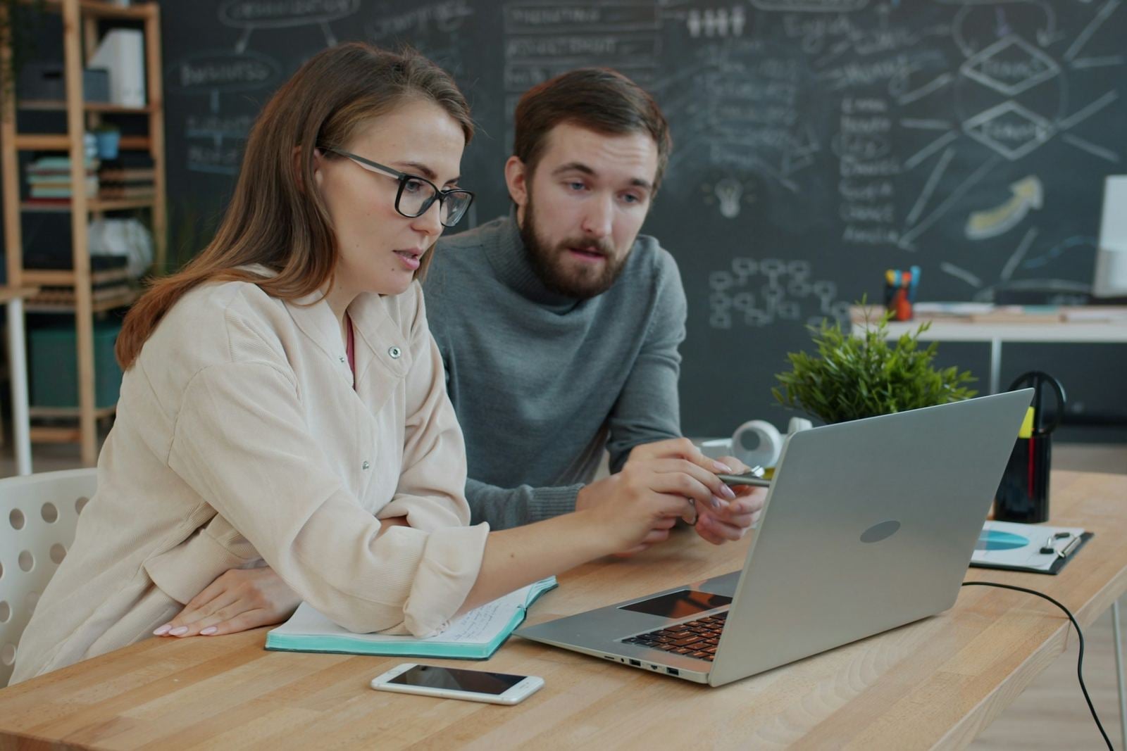 Een ondernemer en een collega bekijken samen iets op een laptop aan een houten tafel in een licht kantoor
