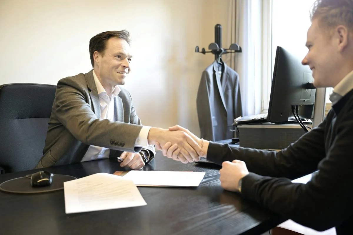 Twee mannen schudden elkaar de hand na het doornemen van documenten aan een bureau