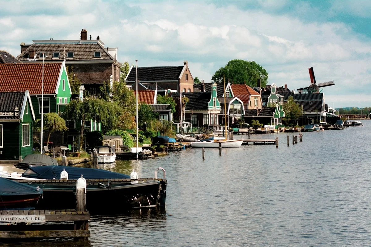 Een Hollandse haven met bootjes, groene houten huizen en een molen aan het water