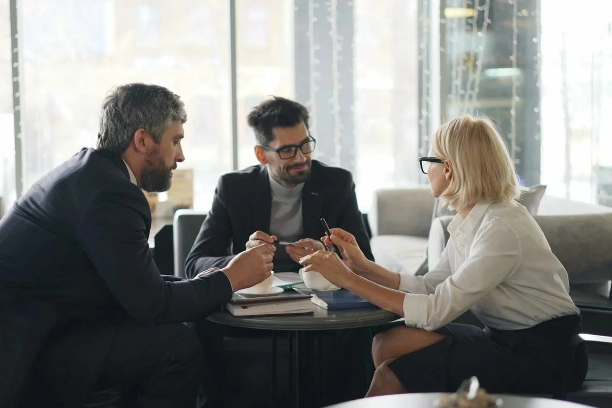 Drie adviseurs bespreken samen een vraagstuk aan een tafel in een licht kantoor