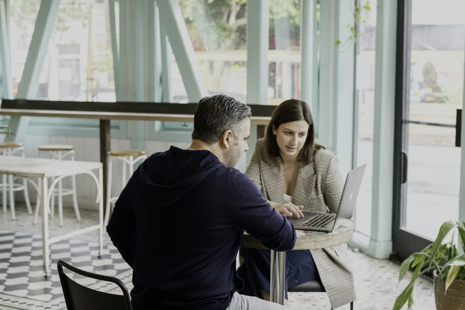Een ondernemer bespreekt de plannen met een professional aan een tafeltje met laptop bij een groot raam