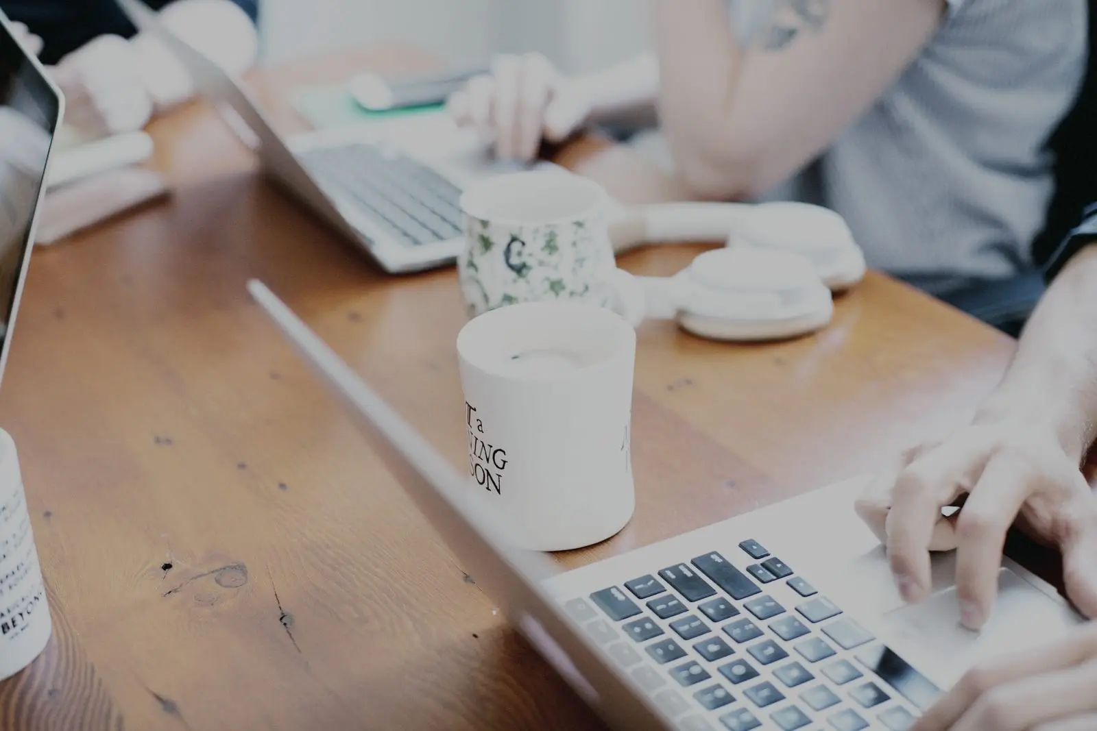 Een kort overleg aan een houten tafel met laptops, koffiemokken en handen op het toetsenbord
