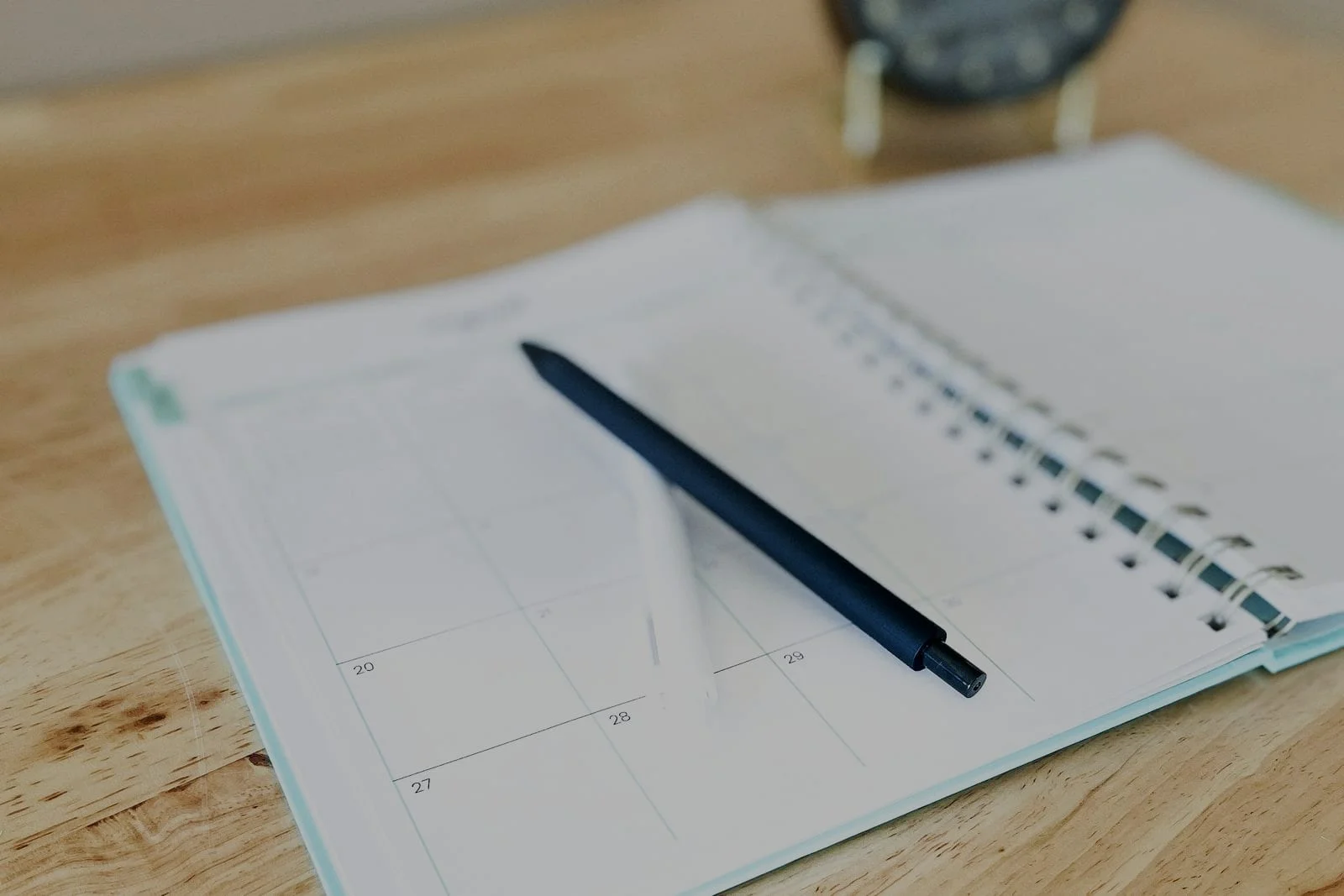 Een opengeslagen maandplanner met een pen op een houten bureau