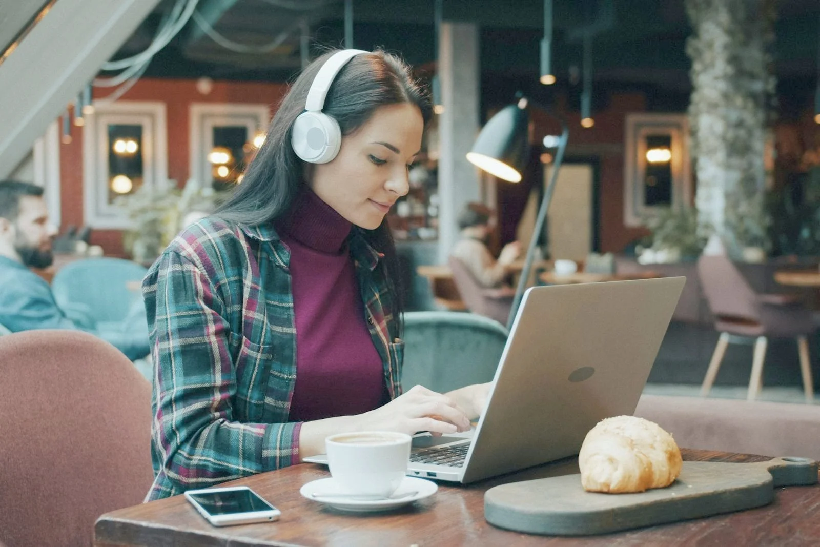 Een zzp’er met koptelefoon werkt ontspannen op haar laptop in een sfeervol café, met koffie naast zich